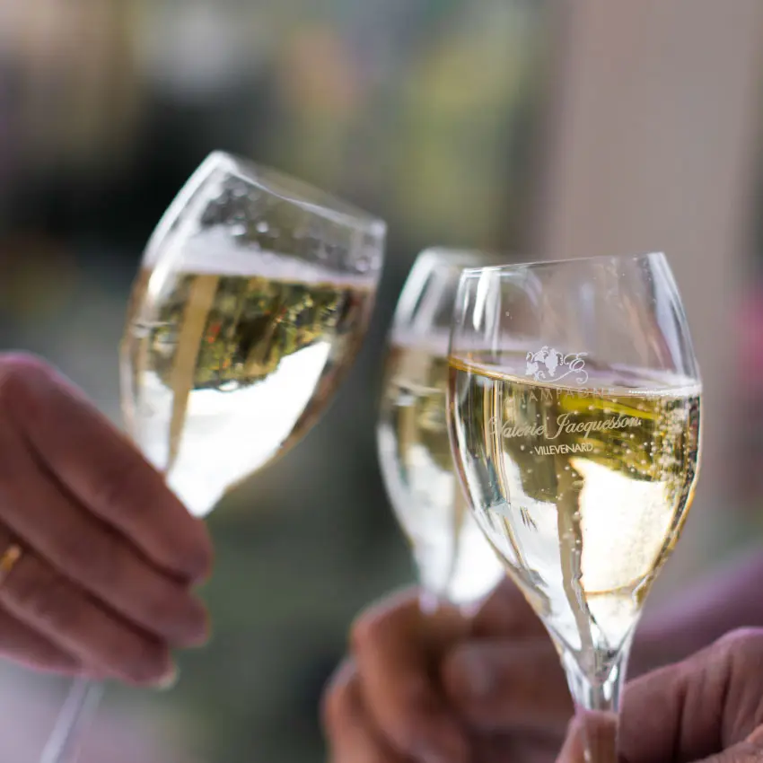 Trois flûtes de champagne trinquent, l'une gravée « Valérie Jacquesson, Villevenard »