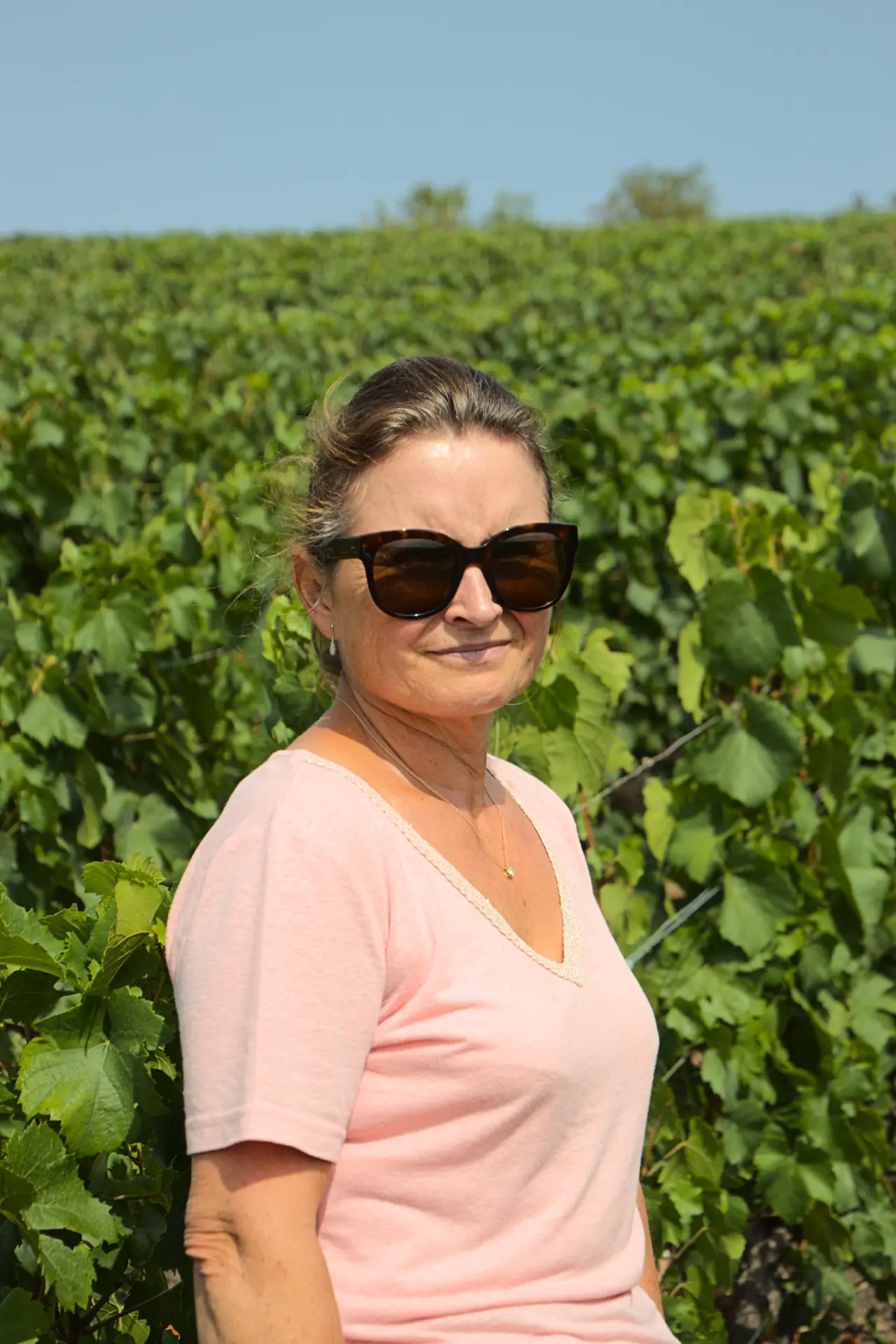 Valérie Jacquesson, lunettes de soleil et haut rose, devant un rang de vigne